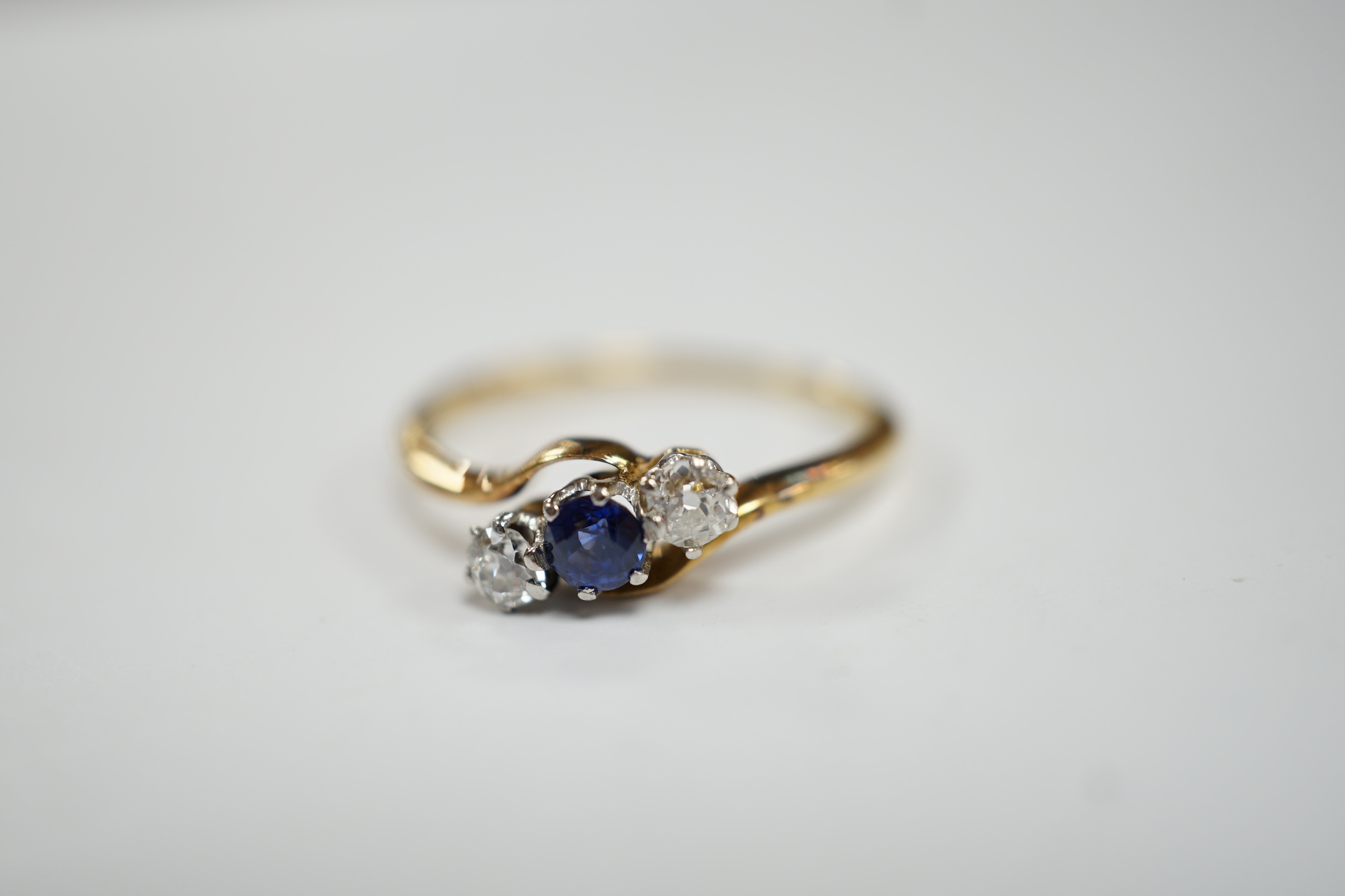 An 18ct, single stone sapphire and two stone diamond set crossover ring, size O, gross weight 2.2 grams.